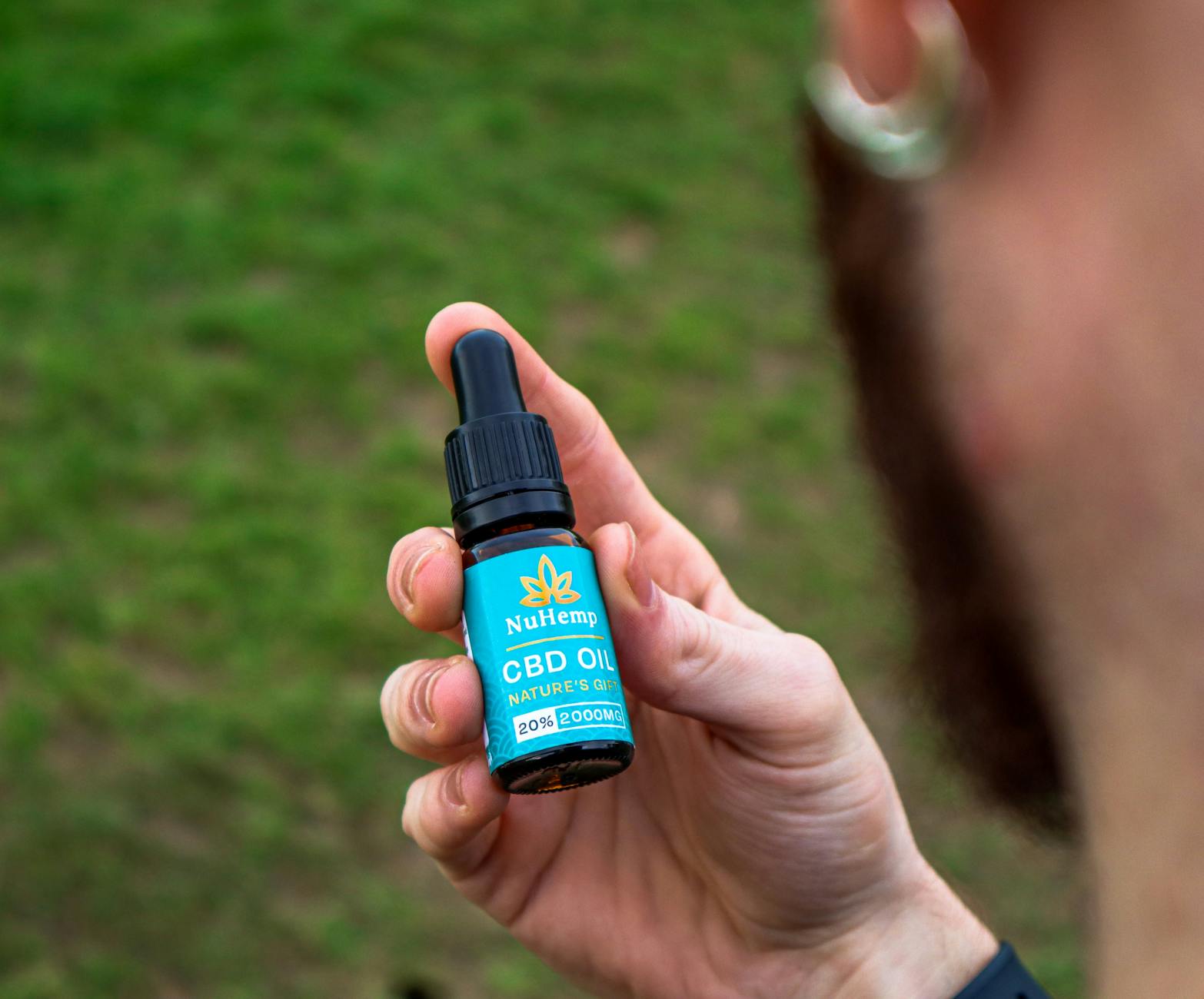 Dłoń trzymająca butelkę olejku CBD NuHemp na tle zielonej trawy