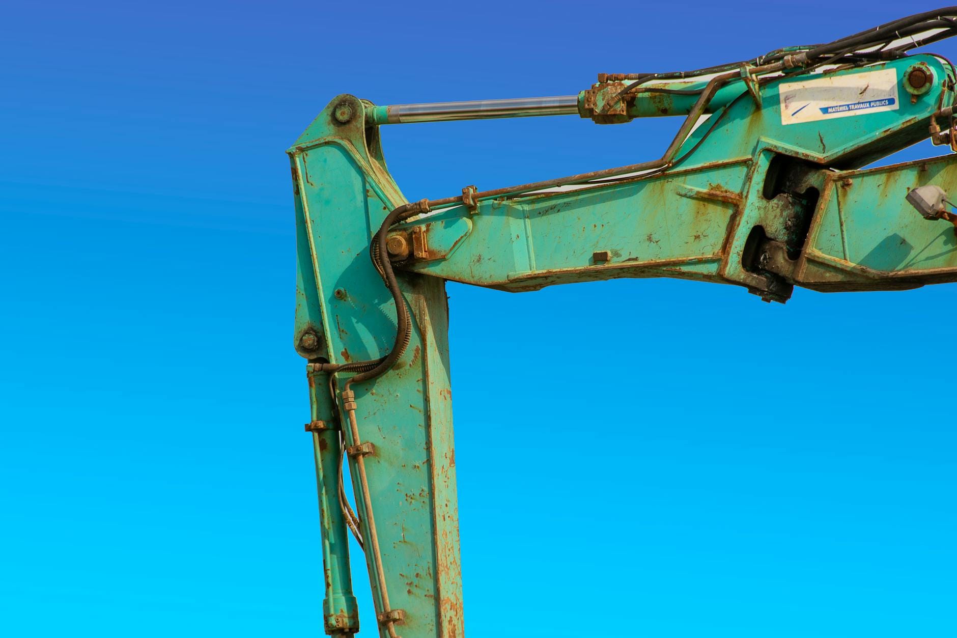 Hydraulika siłowa w przemyśle ciężkim – kluczowe zastosowania i wyzwania Ramię turkusowej koparki hydraulicznej na tle błękitnego nieba