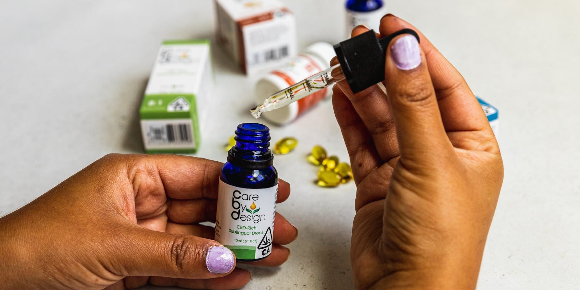 Dłonie z pipetą odmierzające olejek CBD na tle opakowań